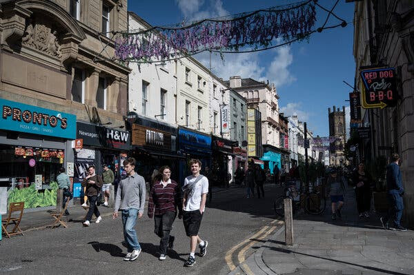 Three young people walking on a sunny street lined with shops and restaurants. 