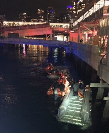 Photo of a small boat with rescue boats nearby with Seattle in background