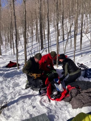 Rangers kneel and help hiker in snowy woods
