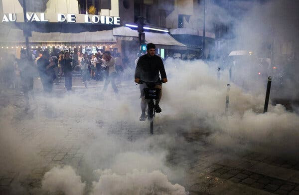 A man riding a bike through clouds of tear gas.
