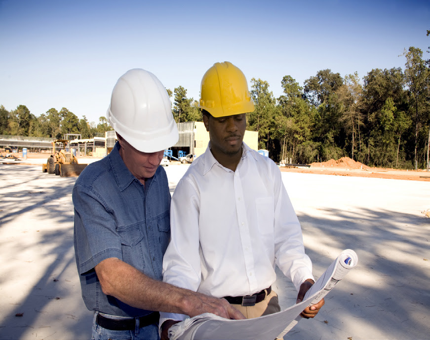 Two men in hard hats look over plans at a construction site.