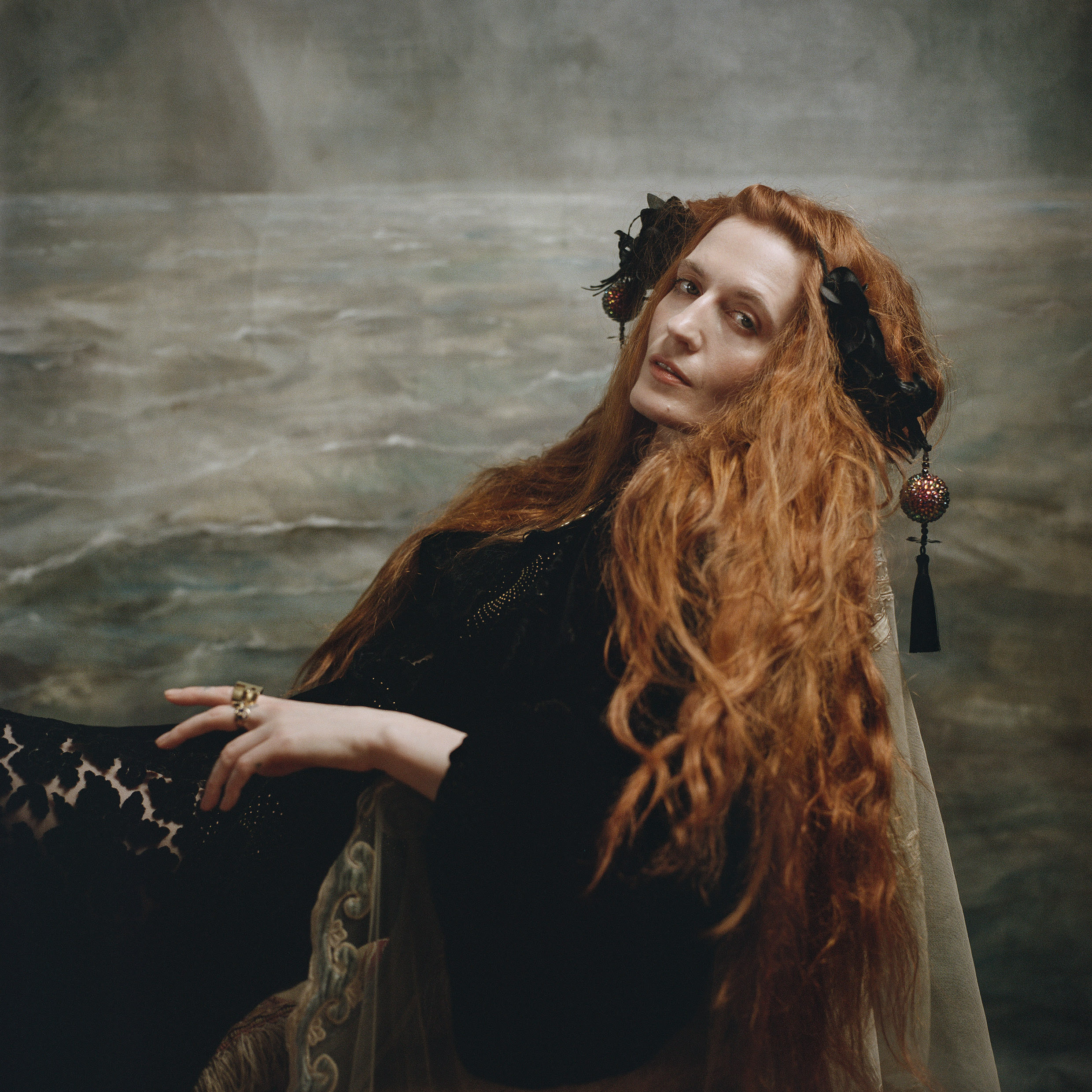 A woman with long red hair looks at the camera with a serious expression.