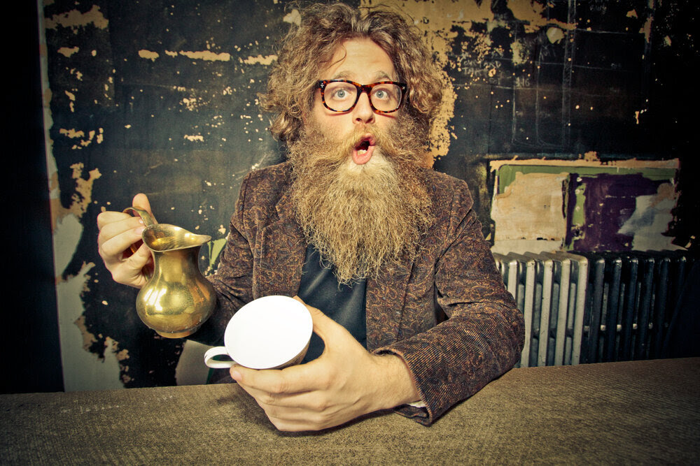 Ben caplan holds a brass tea pot and cup with his mouth open