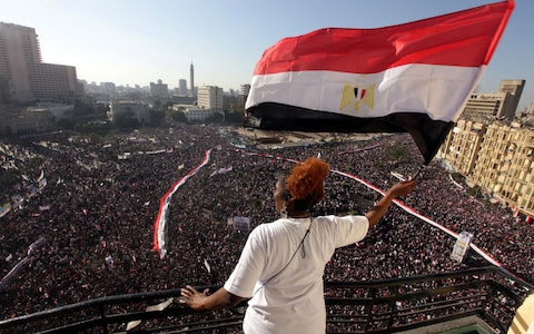 A woman waves an Egyptian national flag from a balcony overlooking Tahrir Square, Cairo on Feb 18, 2011