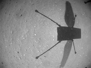 Black and white image taken by Ingenuity helicopter of the Mars surface with the helicopter's shadow.