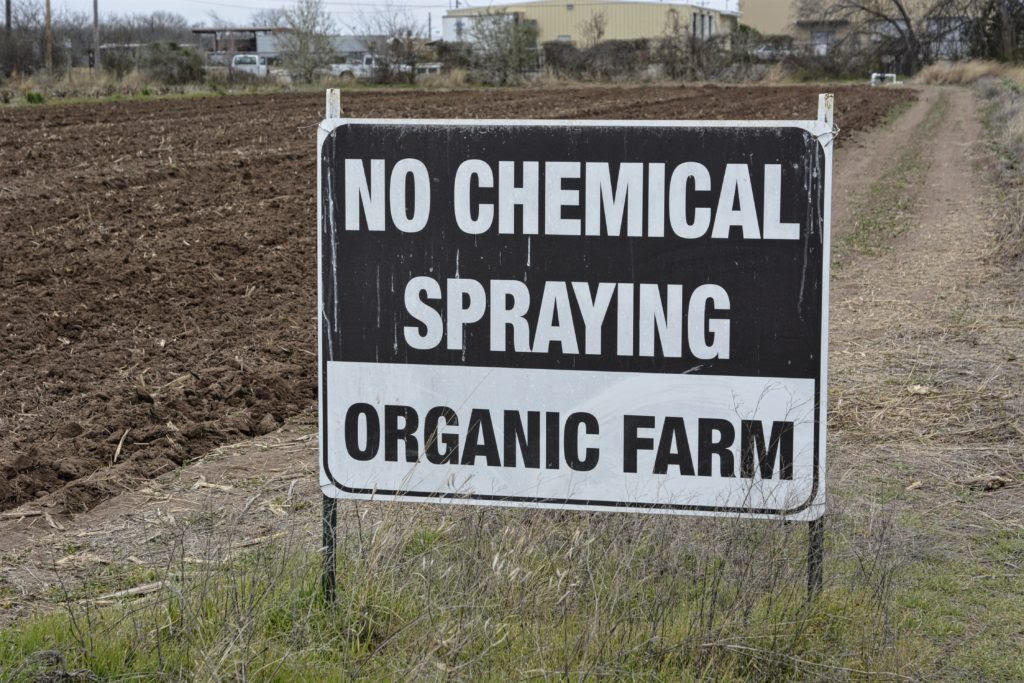 A sign beside a field that says No Chemical Spraying - Organic Farm
