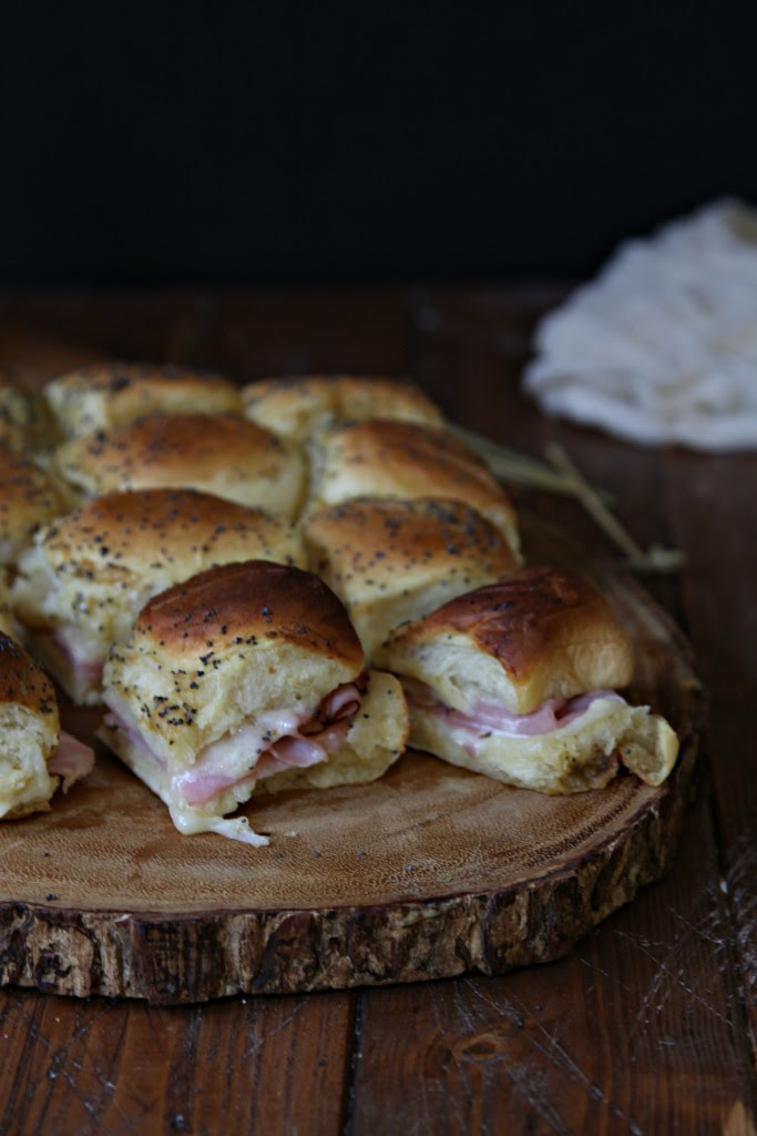 Hot Ham and Cheese Sliders sitting on decorate wood trivet. Cloth napkin in background. 