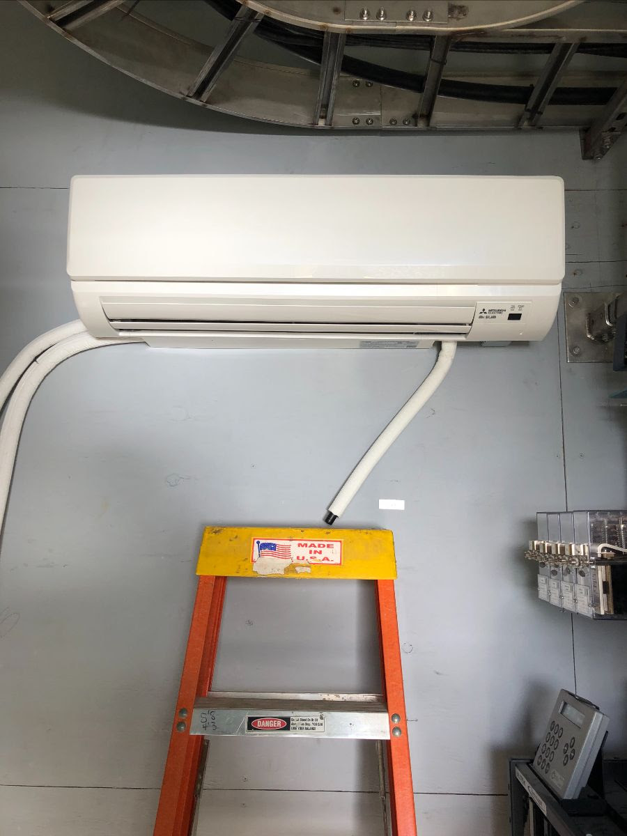 A ductless minisplit heater/cooler is shown attached to a wall of the control tower with a stepladder below it. 