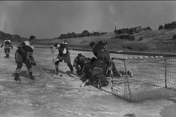 Black & white photo of men playing hockey on outdoor rink.