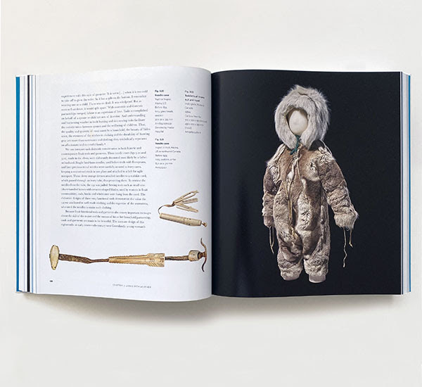 The exhibition catalogue open showing text and an image of a child's snowsuit.