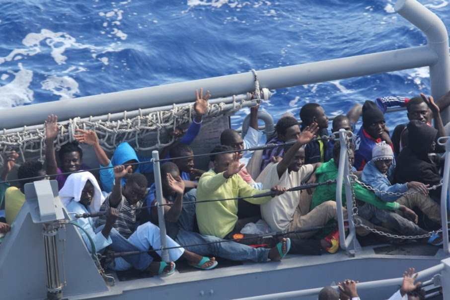 Distressed persons wave after being transferred to a Maltese patrol vessel.