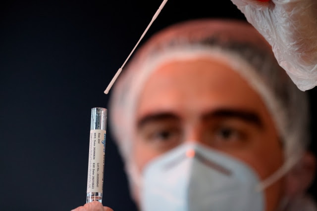 A health worker, wearing a protective suit and a face mask, holds a test tube after administering a nasal swab to a patient in a temporary testing site for the coronavirus disease (COVID-19) at the Zenith Arena in Lille, France, October 26, 2020. REUTERS/Pascal Rossignol