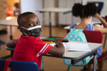 young black boy in mask at desk