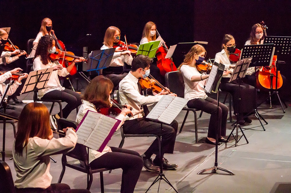Orchestra students wearing masks perform on stage