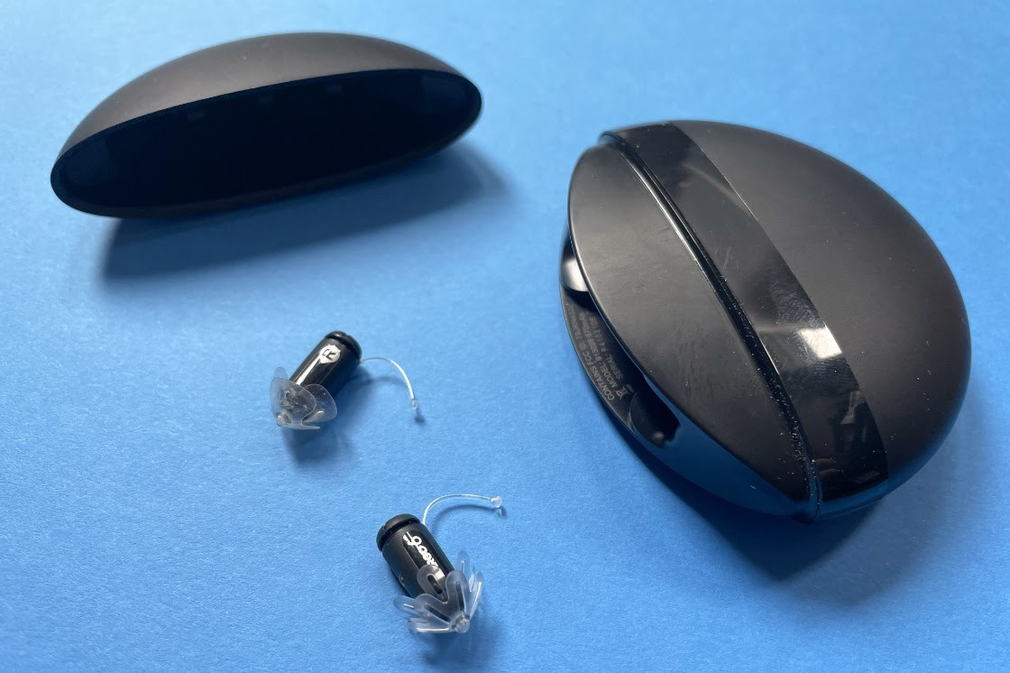 The black Eargo 6 hearing aids and case spread out on a blue table.