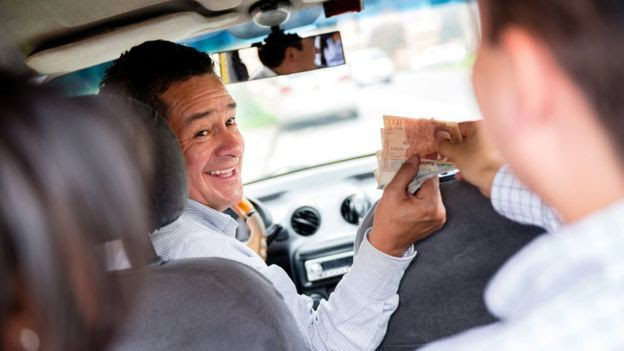 Taxista recibe dinero de un pasajero.