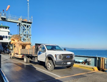 Flatbed truck transporting a wooden troll art sculpture off a ferry at Fauntleroy terminal