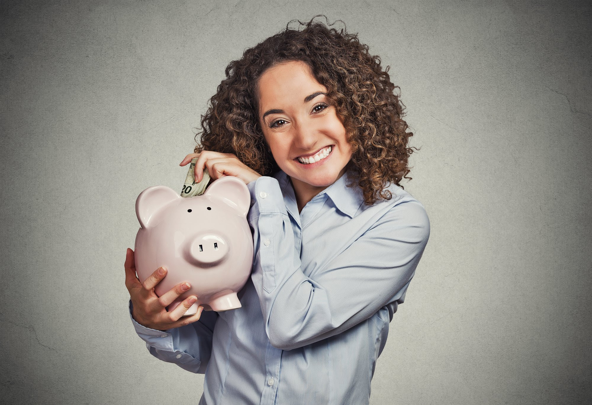 A woman holding a piggy bank and smiling.