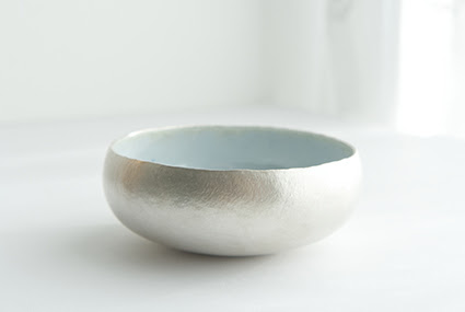 A photograph of a silver and enamel bowl by Emma Louise Wilson. It is displayed on a white background. The outside of the bowl is silver and the inside is blue enamel.