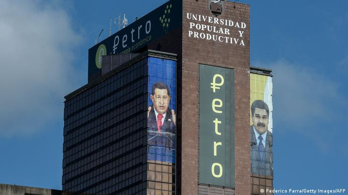 O logotipo da criptomoeda venezuelana Petro aparece entre as imagens do falecido presidente venezuelano Hugo Chávez (esquerda) e do presidente venezuelano Nicolas Maduro em um prédio no centro de Caracas, em 21 de setembro de 2018.