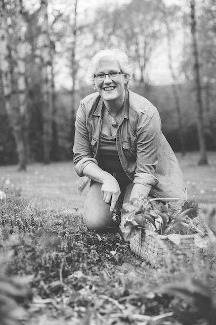 A smiling women kneeling outside in front of a basket of fresh garden cuttings