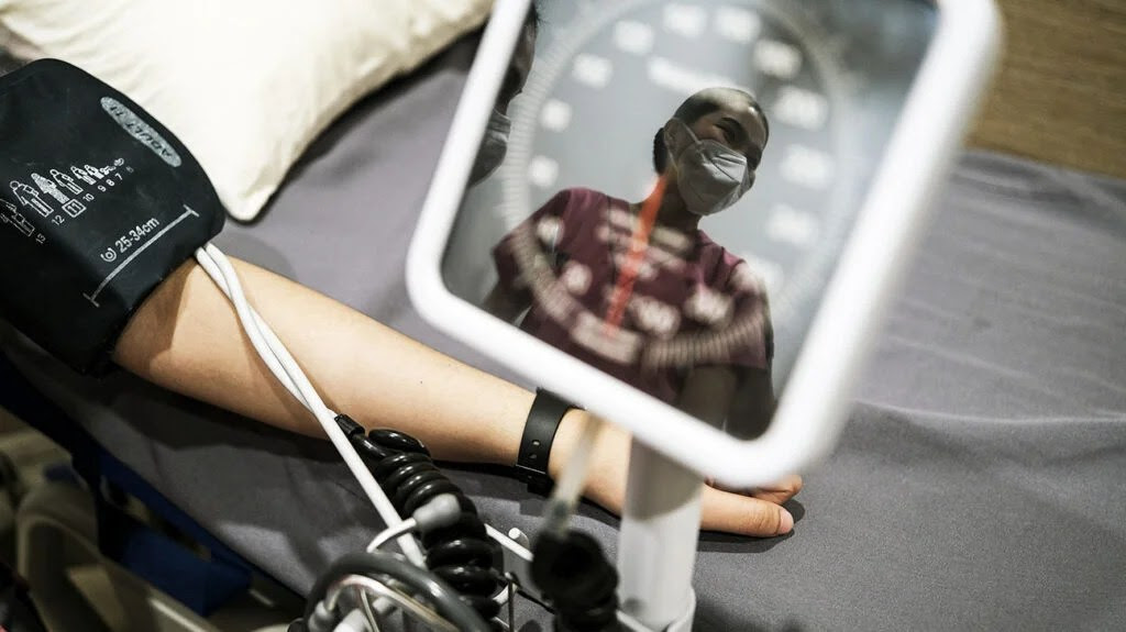 A patient gets their blood pressure monitored as a nurse's reflection is seen on the monitor