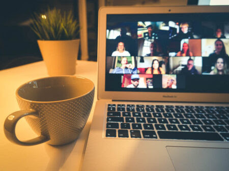 Coffee cup next to computer screen with people in online meeting.