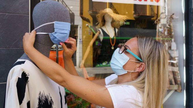 A woman places a mask on a mannequin outside a clothing store in Aranda de Duero, near Burgos on 7 August