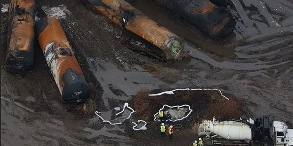 Workers stand in a field of toxic mud, surveying the remains of derailed train cars.