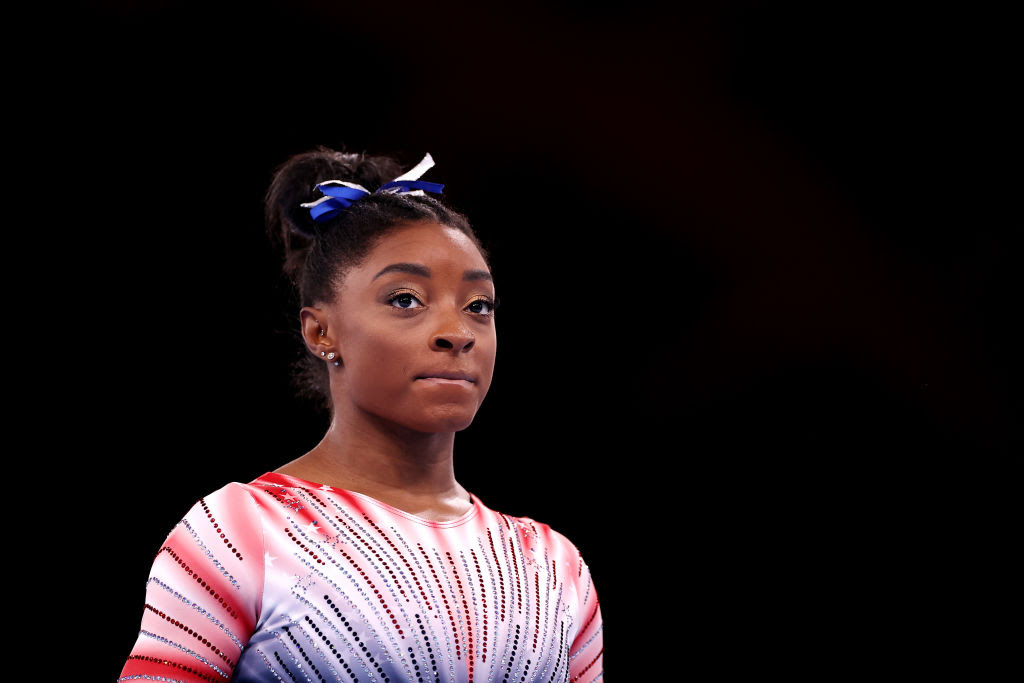 A black athlete with a red suit and a blue ribbon in her black hair.