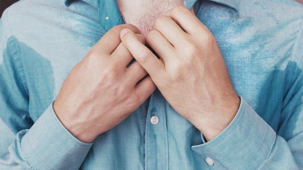 a close up image of a person with sweat patches under their arms which can cause smelly armpits