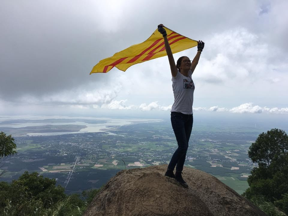 Một cô gái với lá cờ ba sọc đỏ tung bay trên đỉnh núi (ảnh; Facebook Hong Thai Hoang) 