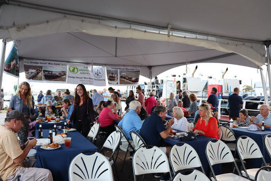 Image of attendees enjoying refreshments seated at tables under a tent.