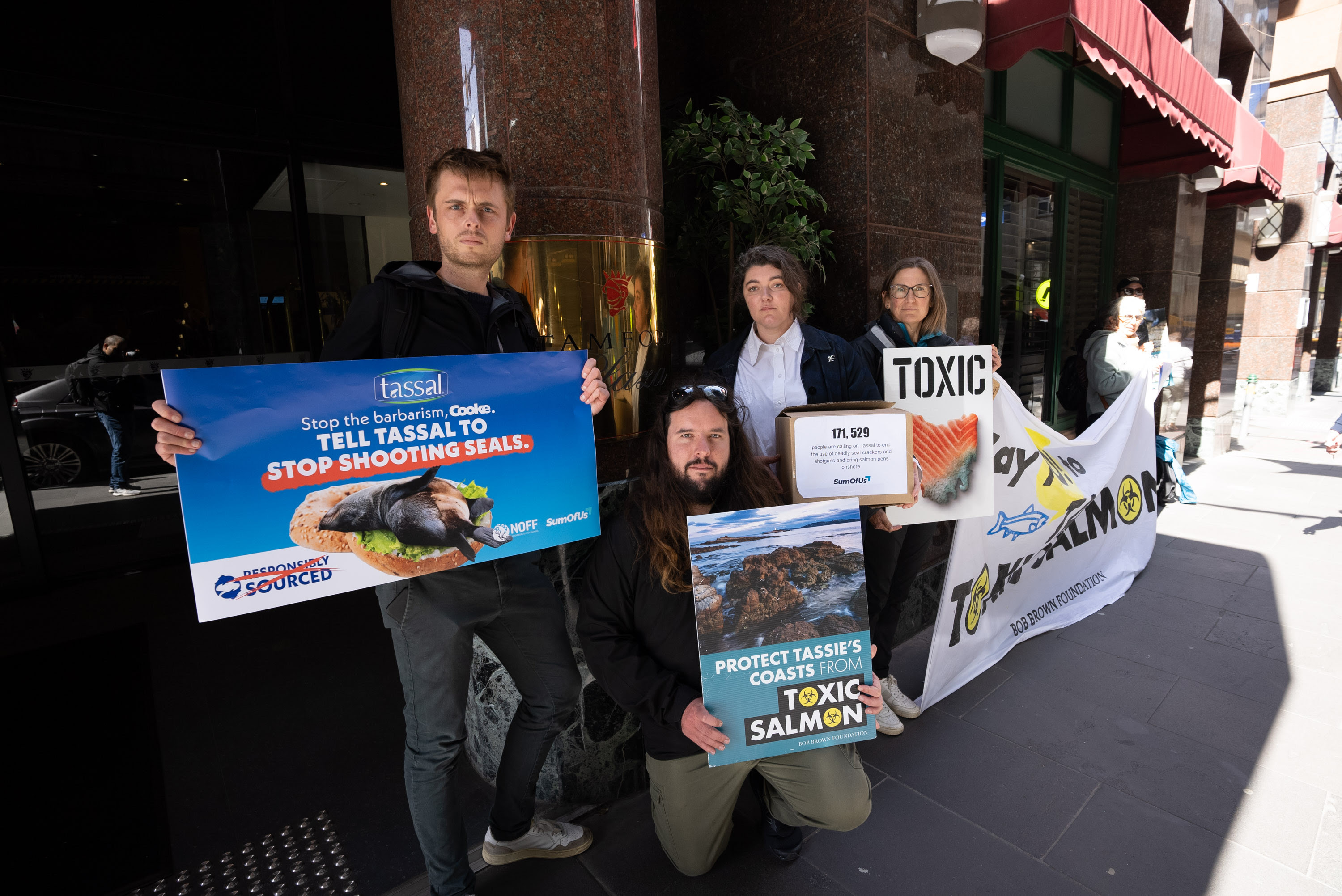 Group of activists hold signs and banners protesting Tassal's toxic salmon industry practices.