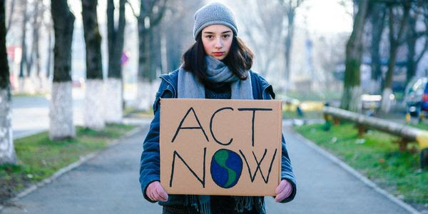 A teenager holding an ''Act Now'' sign, with the ''o'' in ''Now'' colored in to look like the Earth.