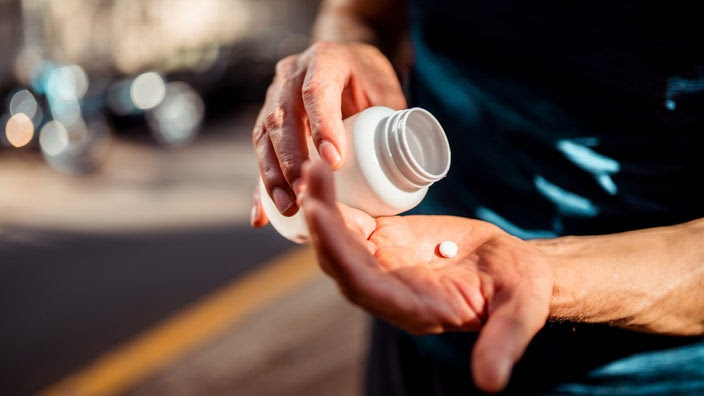 Close-up of a mans’ hands pouring a pill from a bottle into his palm.