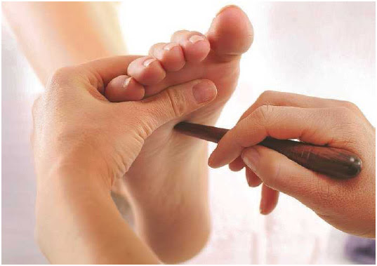 A woman uses a massaging tool to stimulate acupressure points in a person's foot. Acupressure techniques are used to release muscle tension, increase blood flow, and enhance the body's energy.