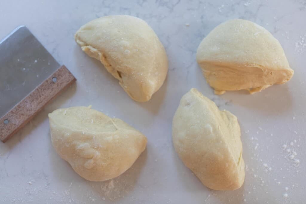 four pieces of sourdough dough on a white countertop with a bench scraper