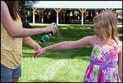 The figure above is a photograph showing an adult female spraying a female child with bug repellent. 