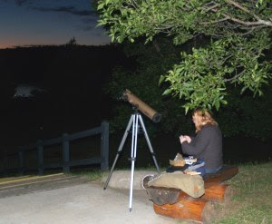 park visitor sits next to telescope near lake