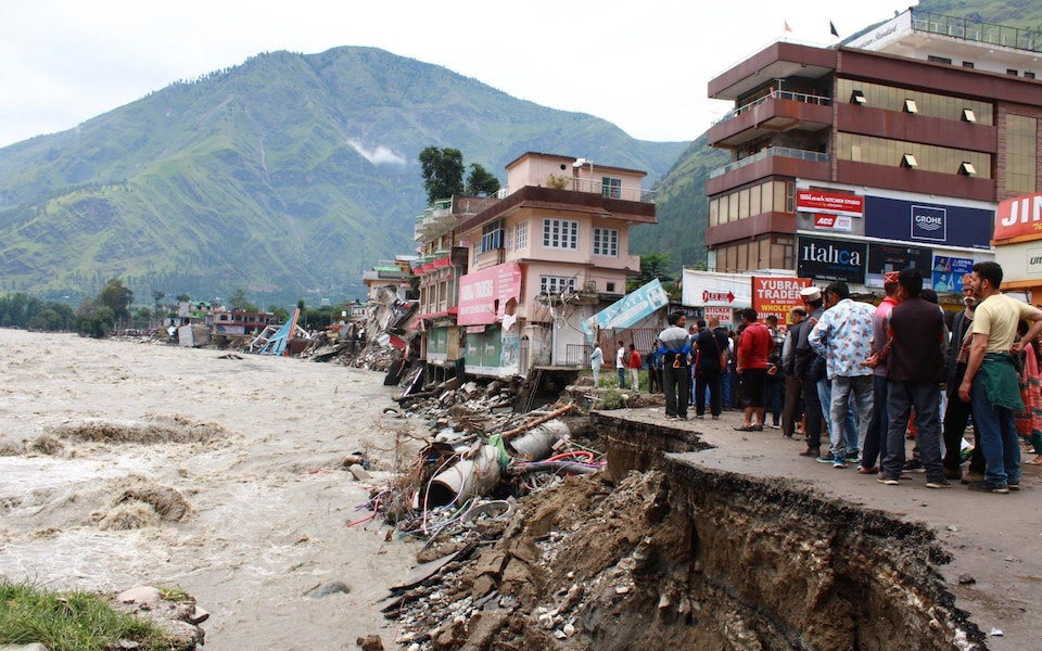 People stand next to a road washed away by the River Beas after heavy rains in Kullu District, Himachal Pradesh