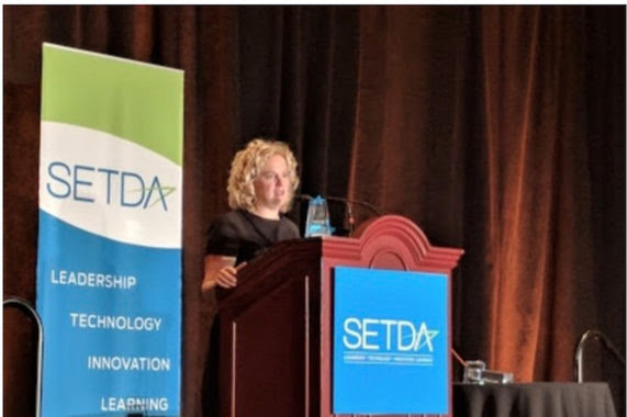 Superintendent speaks from the podium while accepting her award from SETDA during their Leadership Gala. A banner behind her reads, "SETDA, Leadership, Technology, Innovation, Learning"