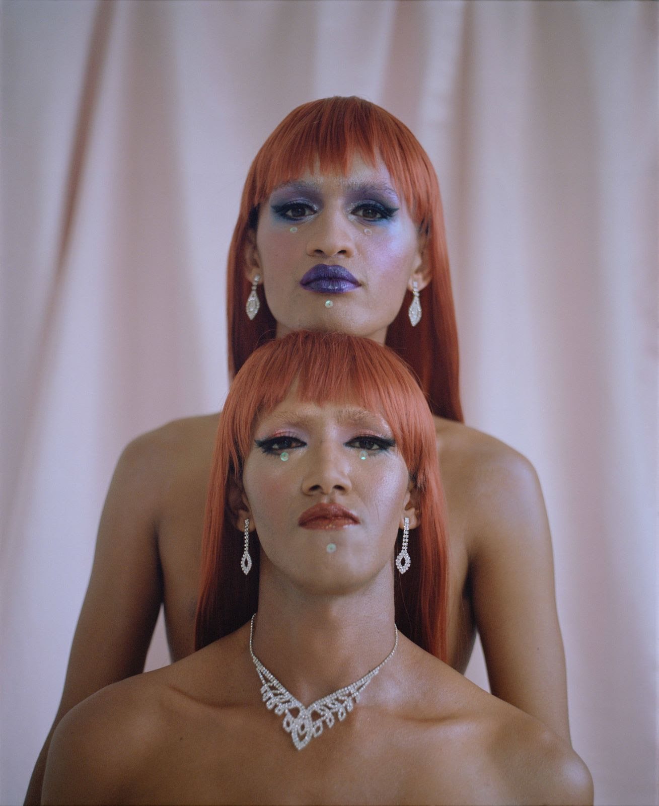 [IMAGE] Photograph showing two trans women topless with long, straight red hair, and blue makeup. One is stood in front of the other and they are both looking straight into the camera.