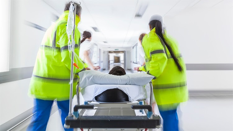 The figure shows a patient on a stretcher being pushed quickly through a hospital corridor by health care providers.