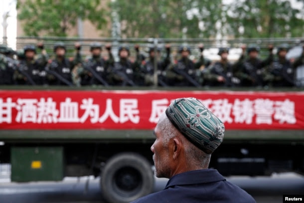 FILE - A Uighur man looks on as a truck carrying paramilitary policemen travels along a street during an anti-terrorism oath-taking rally in Urumqi, Xinjiang Uighur Autonomous Region.
