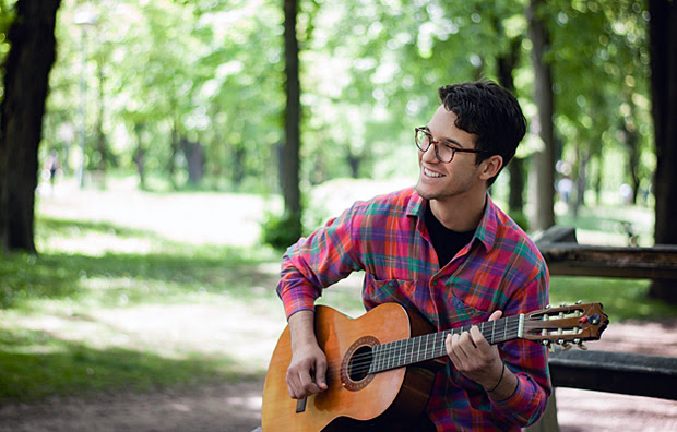 A young man playing a guitar in the park.