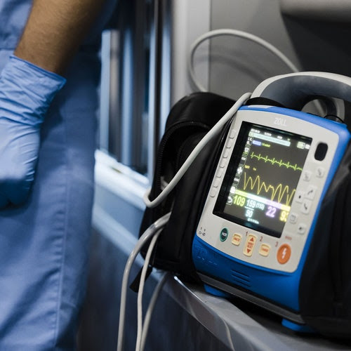 A person wearing scrubs stands next to a vital-signs monitor in an ambulance.