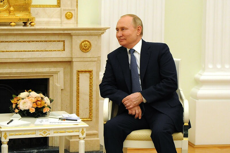 Presidente da Federação Russa, Vladmir Putin, durante reunião com governo brasileiro; Putin é um homem branco na faixa dos 60 anos, com olhos e cabelos claros, ele veste um terno preto; Putin está sentado em uma cadeira olhando para o lado esquerdo