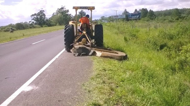 Na foto, um trator com roçadeira faz o corte da vegetação às margens da ERS-030