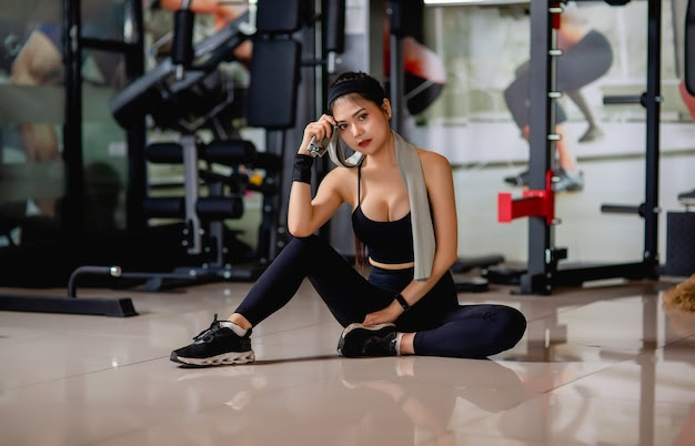 Portrait young sexy woman wearing sportswear and smartwatch sitting on floor and wipe sweat after workout at gym,